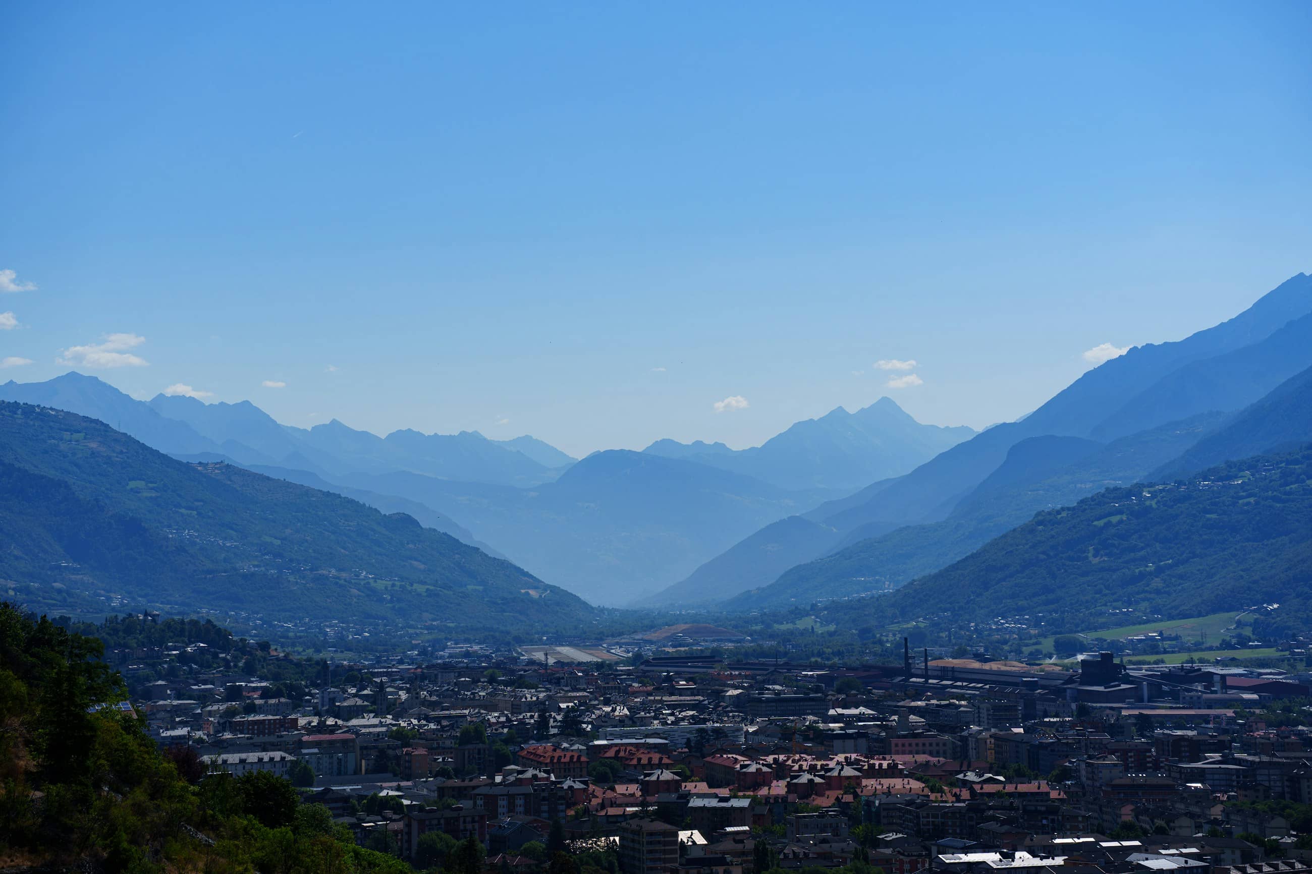 An Alpine valley in afternoon haze, the town spread along its floor and ridges receding behind.